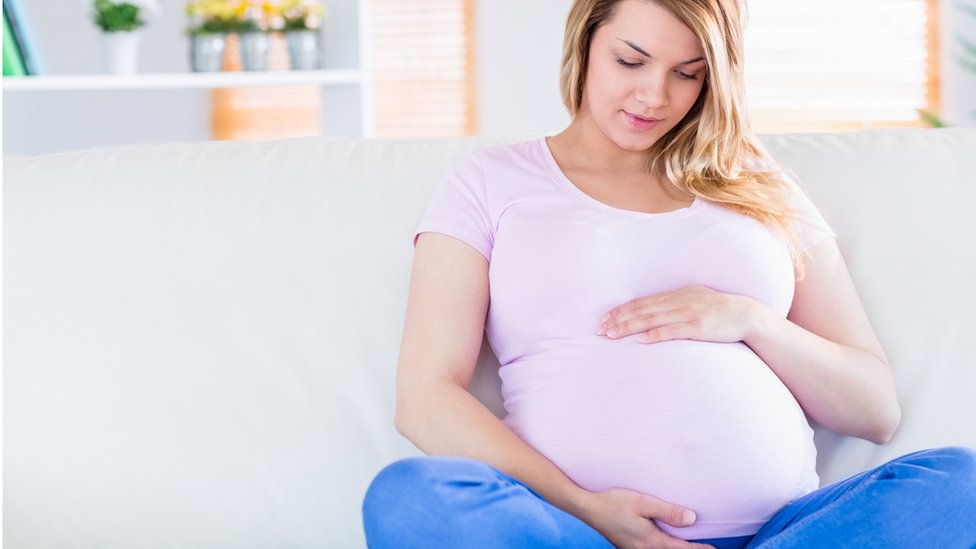 Pregnant woman sitting on a sofa holding her belly