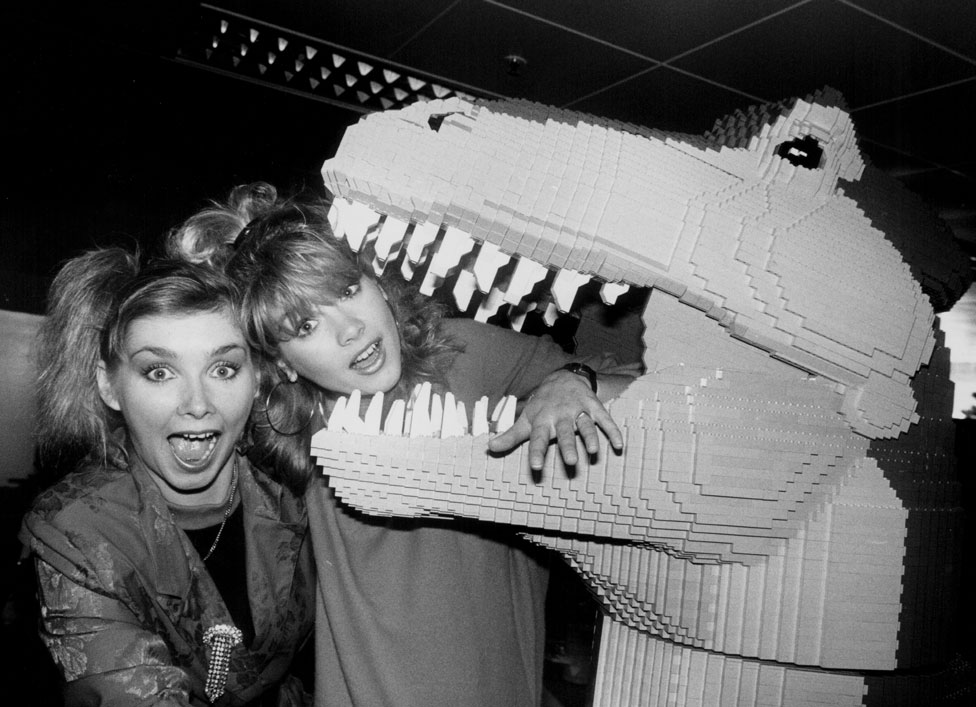 Два певца позируют с динозавром из Lego