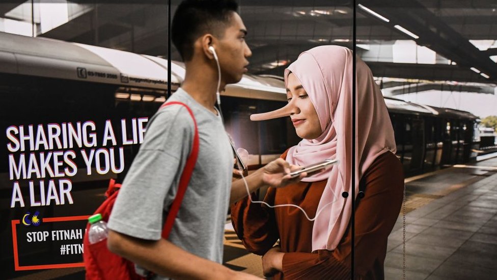 Prolaznik pored reklame na kojoj piše „šerovanjem laži postajete lažov" na železničkoj stanici u Kuala Lumpuru