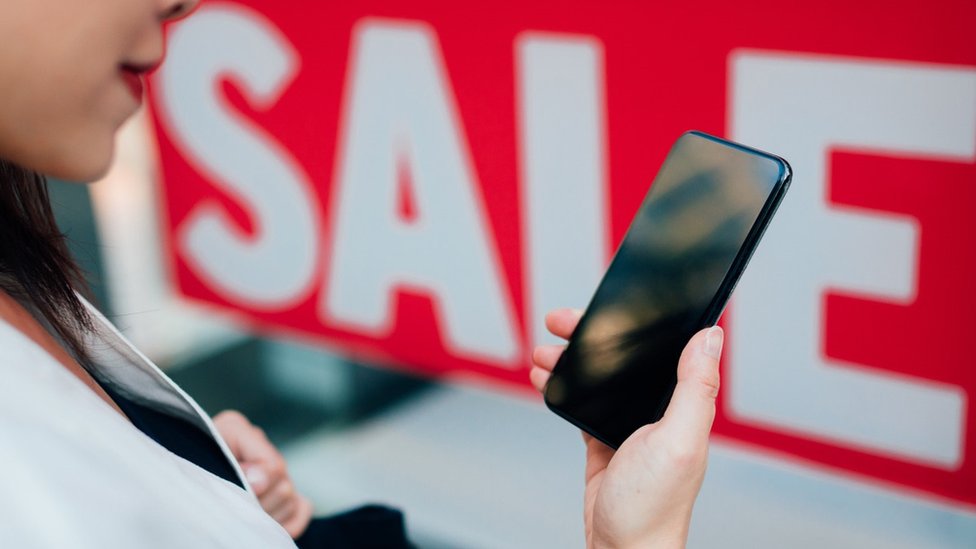 Woman with phone next to sale sign