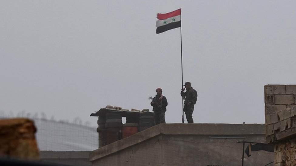 Şam ordusunun askerleri, SDG kontrolündeki Menbic'de bir binaya Suriye bayrağı çekerken görülüyor