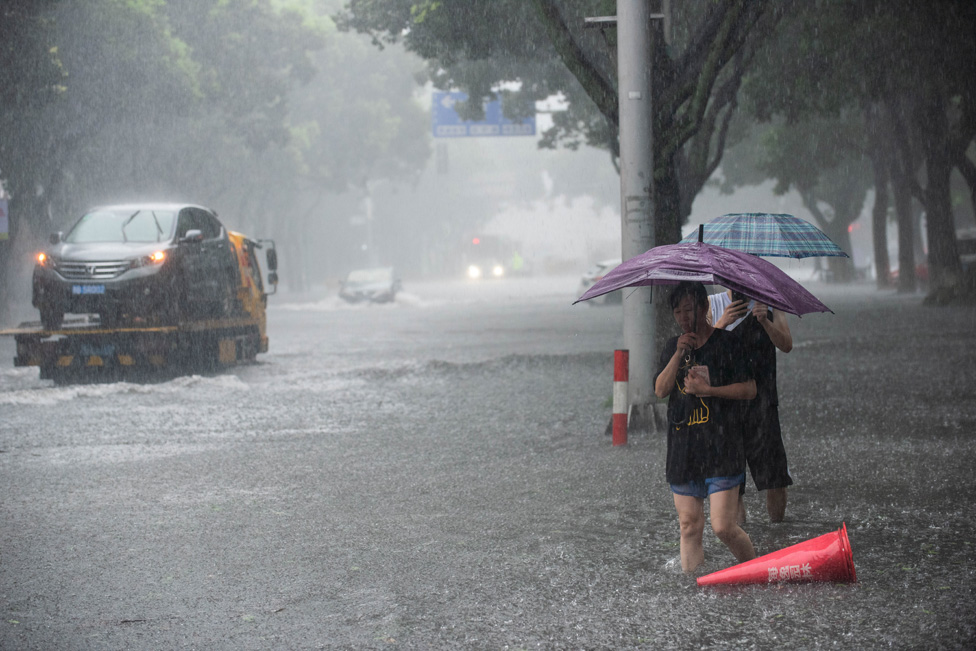 Warga memegang payung berusaha menyeberang jalan melalui banjir di tengah hujan lebat setelah topan dahsyat Lekima mendarat di Ningbo.