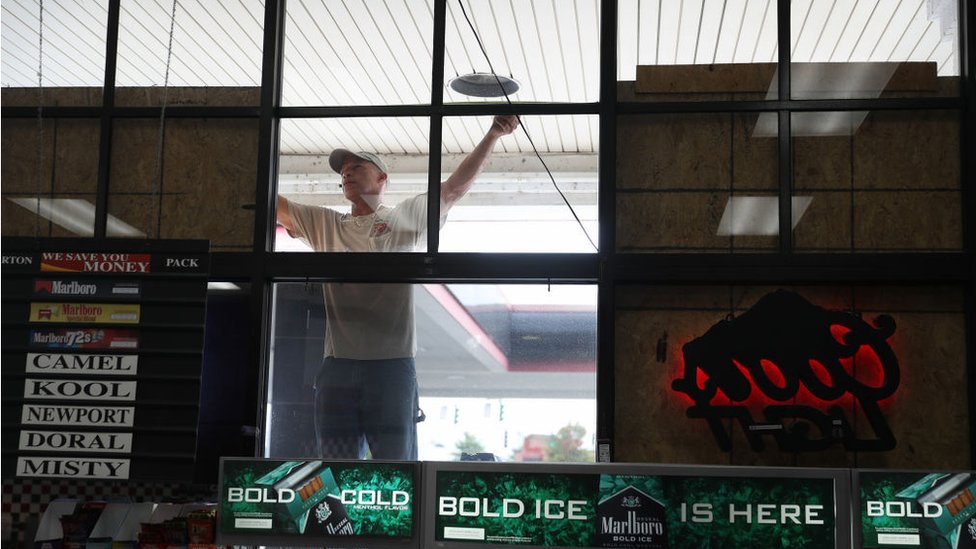 Уэсли Джейкобс измеряет пространство для фанеры, когда он помогает заколачивать окна в бизнесе перед возможным прибытием урагана Лаура 25 августа 2020 г.