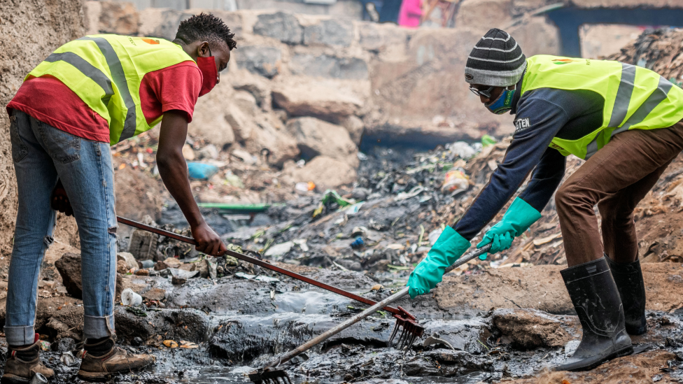 Personas que trabajan bajo un plan del gobierno para limpiar alcantarillas abiertas en Kibera, Kenia