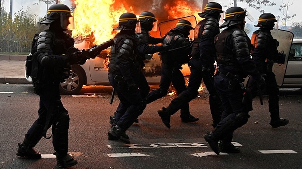 Французский спецназ пробегает мимо подожженного автомобиля во время протестов против желтых жилетов