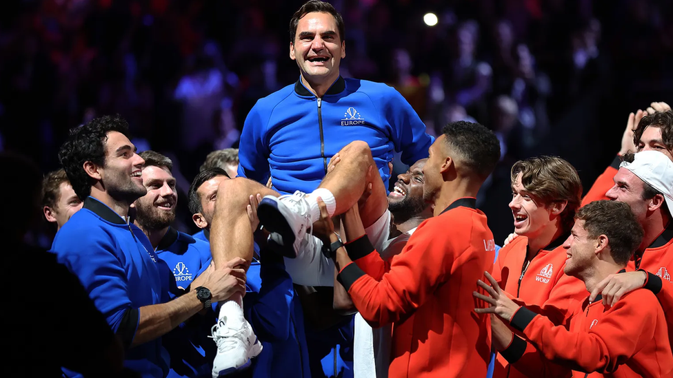 Roger Federer sendo erguido por jogadores