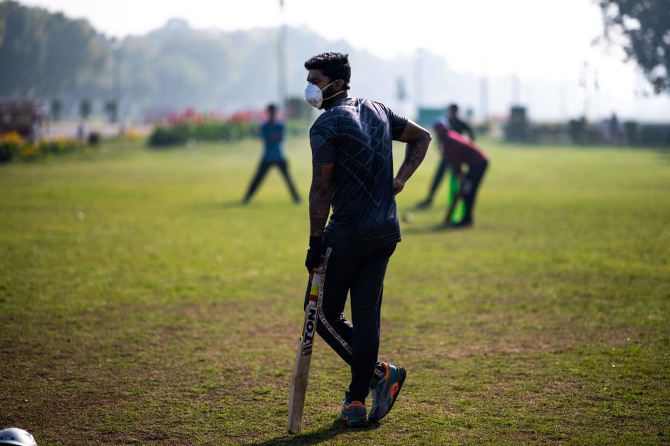 Юноша (C) в маске в качестве профилактики коронавируса COVID-19 играет в крикет со своими друзьями в парке в Нью-Дели 18 марта 2020 года.