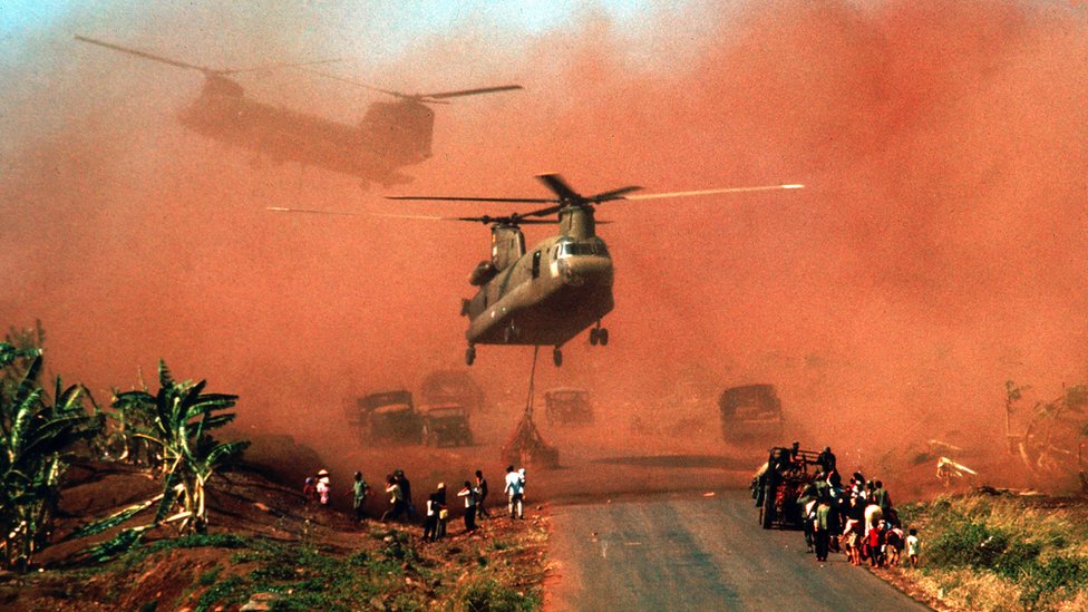 Two Chinook helicopters hover above a road as they assist in evacuating supplies and soldiers of the South Vietnamese (ARVN) 18th Division and their families from Xuan Loc, Vietnam, mid April, 1975.