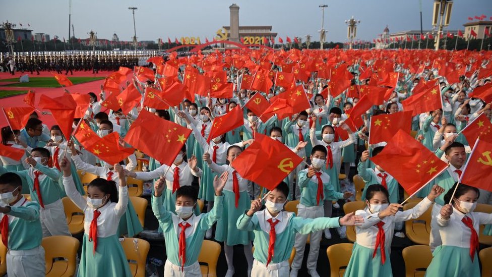 Students wave Chinese flags before the celebration of the 100th anniversary of the founding of the Communist Party of China at Tiananmen Square in Beijing on July 1, 2021.