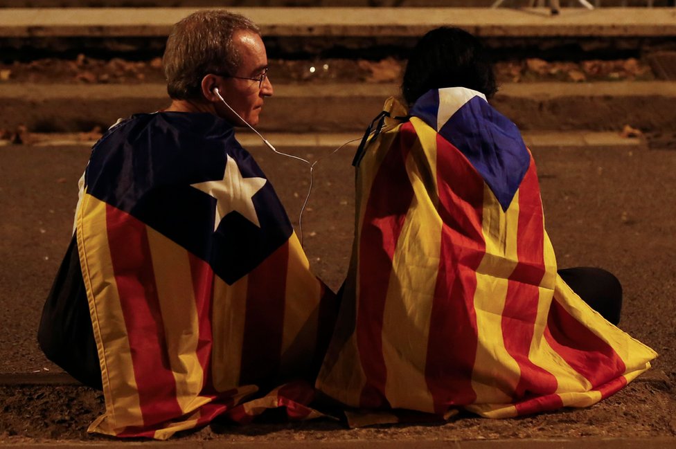 El ambiguo discurso de Carles Puigdemont de este martes fue seguido por miles de personas en las afueras del parlamento regional, que celebraron durante solo unos segundos lo que consideraron era una declaración de independencia. Dos personas siguen por radio la comparecencia de Carles Puigdemont el 10 de octubre de 2017