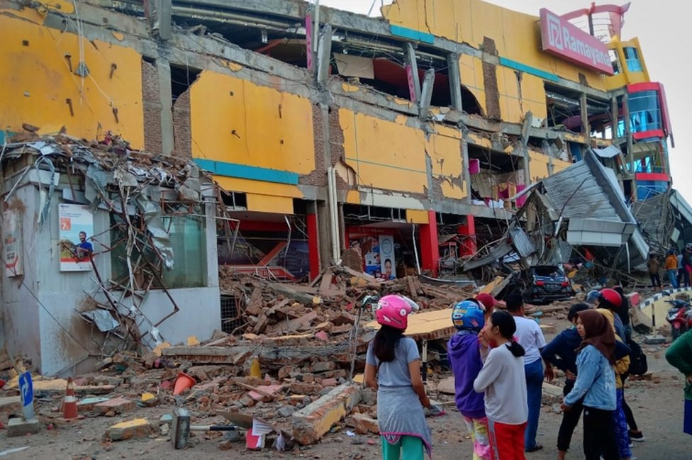 Люди стоят перед поврежденным торговым центром после землетрясения в городе Палу на острове Сулавеси в Индонезии