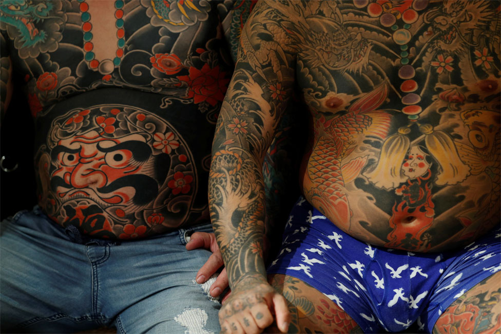 Двое мужчин сидят рядом друг с другом с сильно татуированными торсами