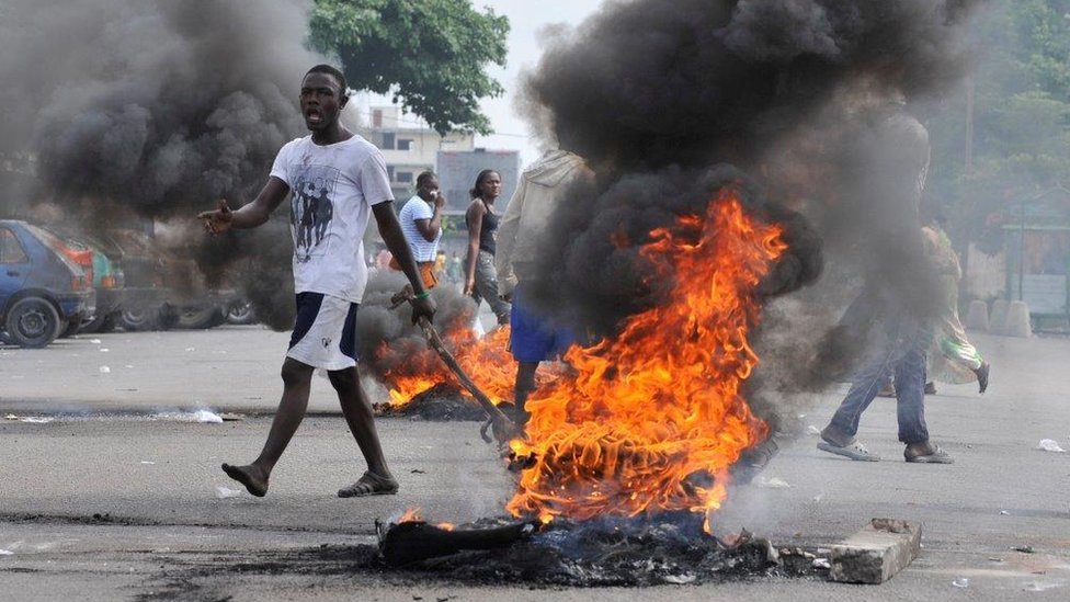 Мужчина стоит у горящей покрышки во время беспорядков после выборов в Кот-д'Ивуаре в 2010 году