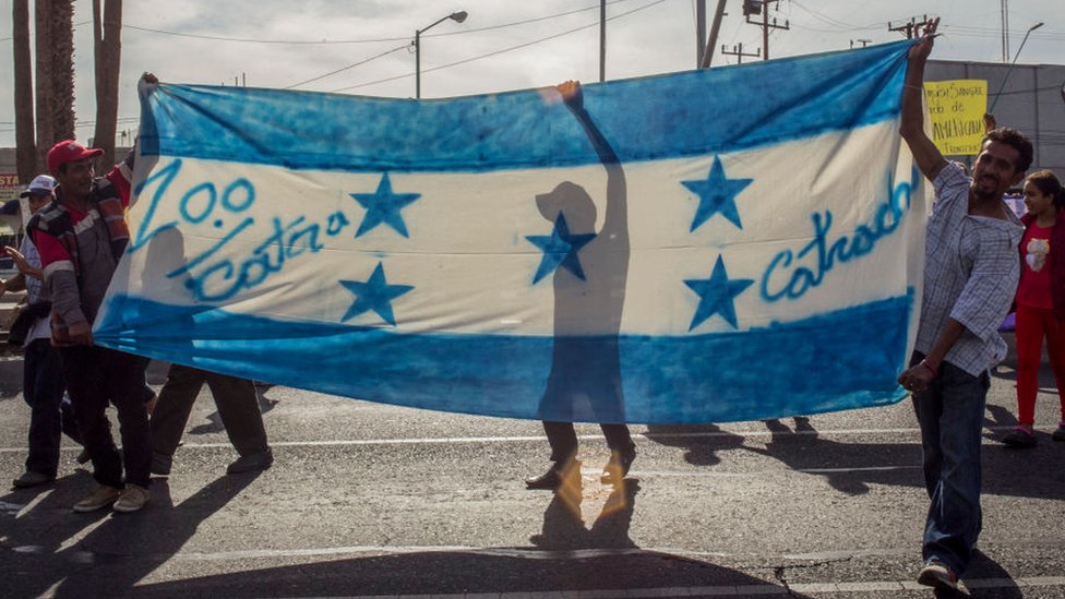 Migrantes con bandera de Honduras y el lema "100% catrachos".