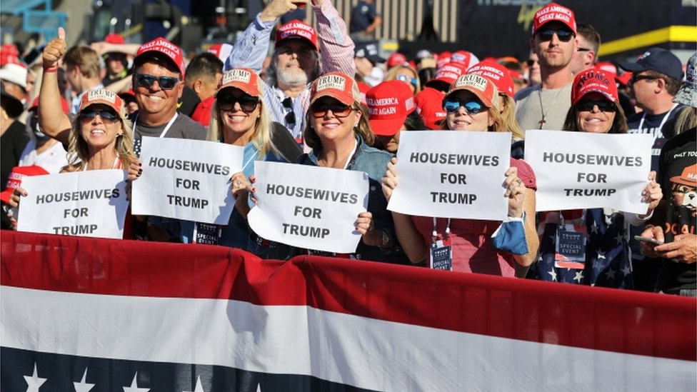 Женщины на митинге в Аризоне 28 октября 2020 года держат домохозяек перед знаками Трампа