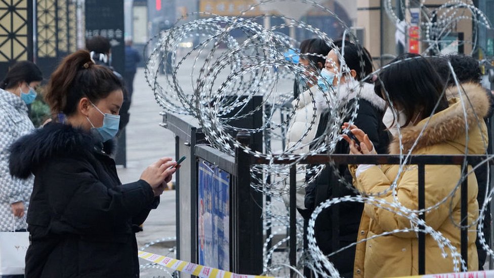 Moradores de Xi'an ficam ao lado de portão com arame farpado