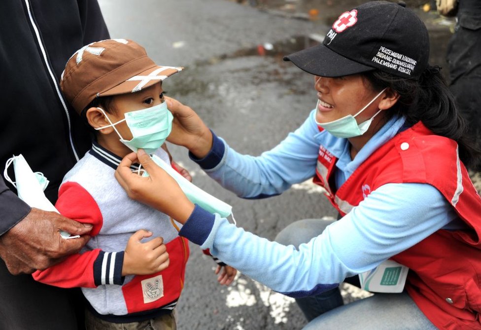 Esta vez, unas 40.000 personas ya han sido evacuadas de la zona de peligro. Pero las autoridades de Indonesia dicen que otras 100.000 tendrán que ser puestas a salvo. Una voluntaria le pone una mascarilla a un niño.