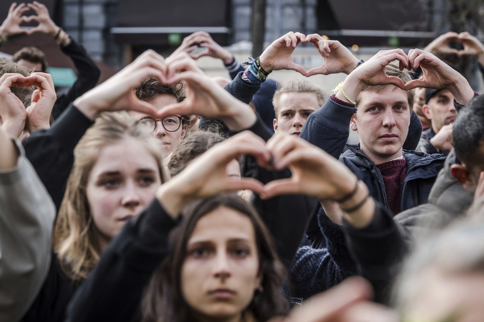 Люди лепят руками форму сердца, стоя на минуту молчания у биржи во время годовщины жертв нападений в Брюсселе, 22 марта