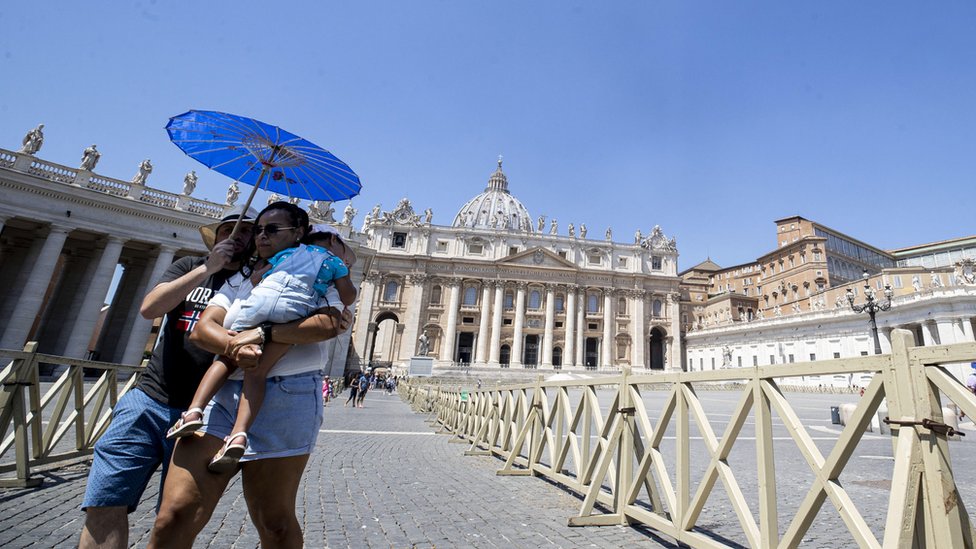 A couple with a child try to protect themselves against the sun with a parasol as they walk near the Vatican