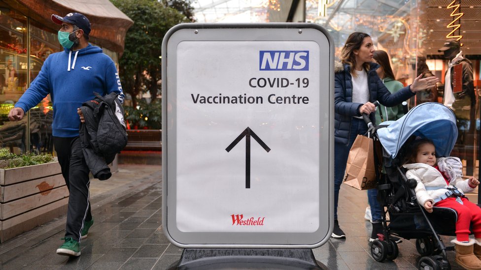 People passing by the NHS covid-19 vaccination Centre direction sign in Westfield Shopping Centre.