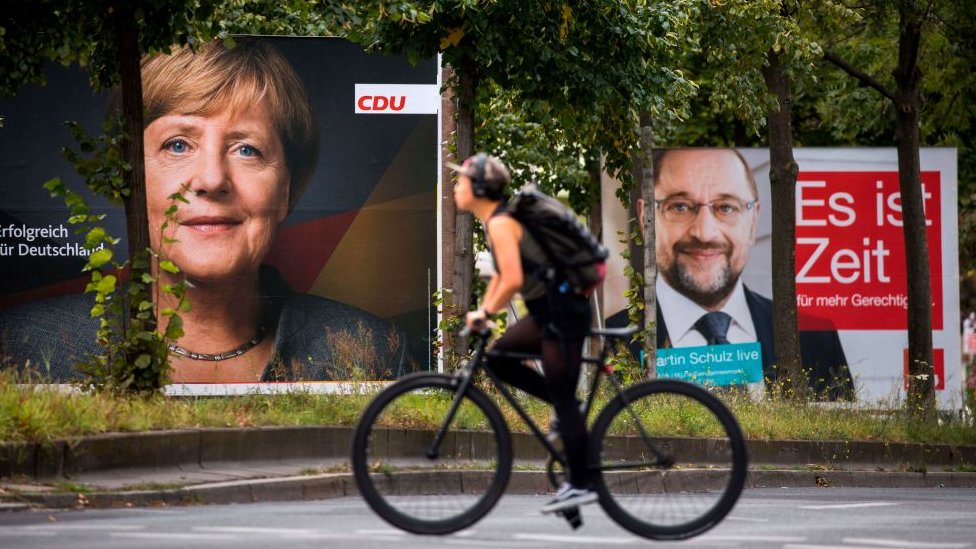 Las encuestas dan como favorita a Merkel. Un ciclista pasa junto a dos carteles electorales con imágenes de Merkel y Schulz en una calle de Berlín.