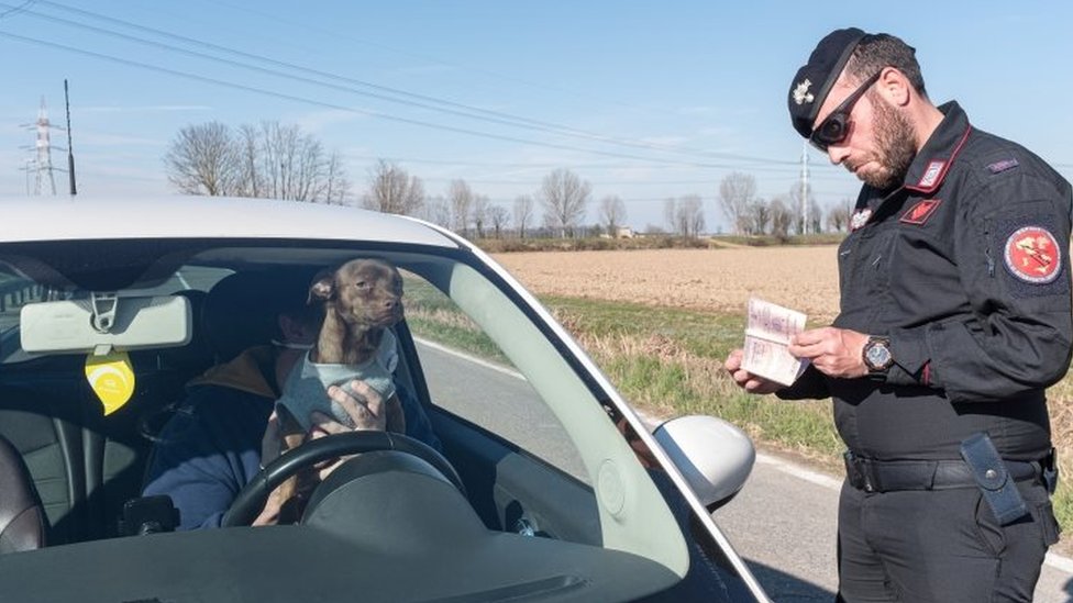 Полицейский проверяет документы мужчины в машине на контрольно-пропускном пункте в Сан-Фьорано, Италия. Фото: 8 марта 2020 г.