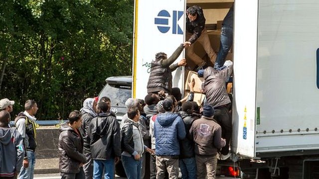 Migrants climb in the back of a lorry on the highway leading to the Eurotunnel
