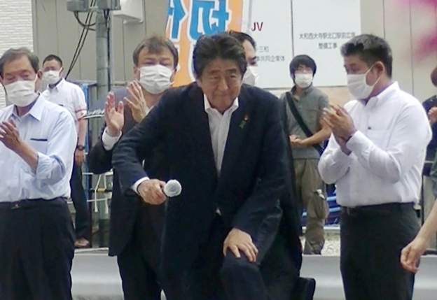 Shinzo Abe, momentos antes de ser baleado. El sospechoso se ve en el fondo con un cinturón atravesado.