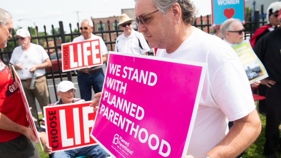 Сторонник программы «Планируемое отцовство» стоит рядом с демонстрантами против абортов, когда они проводят акцию протеста у Центра услуг репродуктивного здоровья «Планируемое отцовство» в Сент-Луисе, штат Миссури, 31 мая 2019 г.