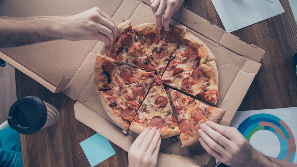 Empleados comparten pizza en la oficina.