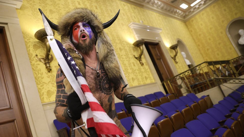 A man in horns and a fur hat, alleged to be Jake Angeli, pictured inside the Senate chamber