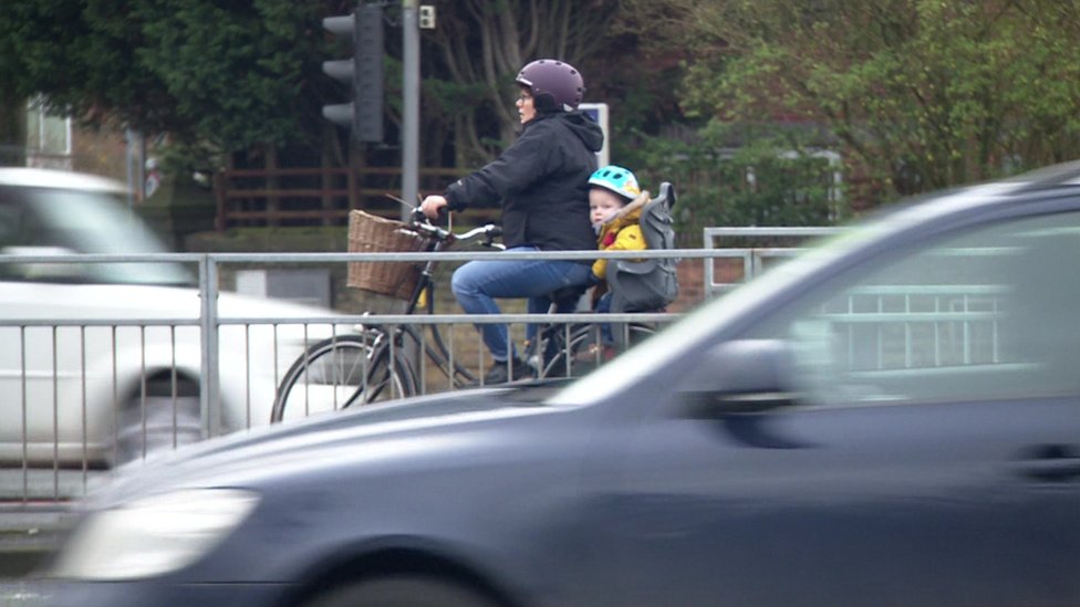 Женщина катается на велосипеде с ребенком в условиях интенсивного движения
