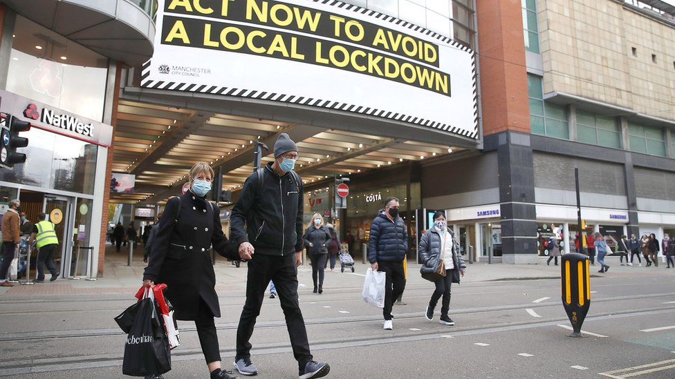 People wearing face masks walk past a advertisement on Market Street in Manchester