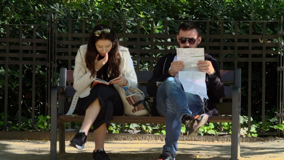 A man and a woman sit on a bench reading