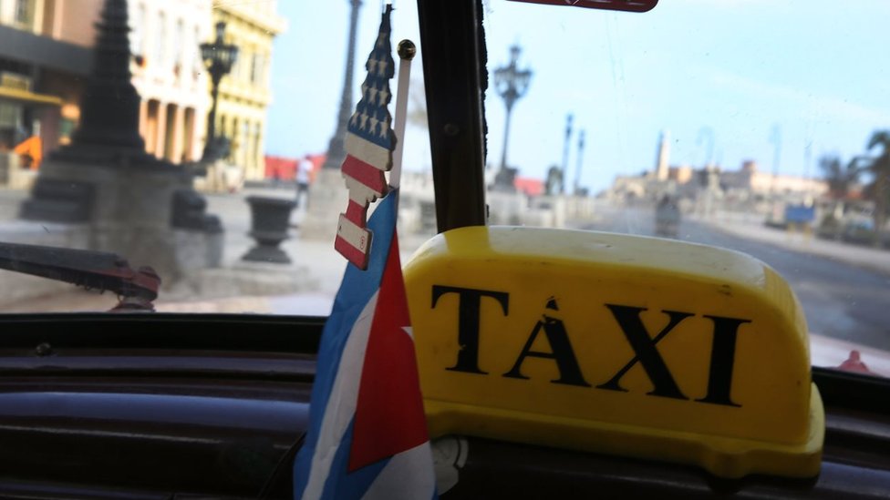 El número de turistas que viajan a Cuba ha aumentado en niveles récord desde 2014. La vista desde dentro de un taxi en La Habana. El aromatizador que cuelga del espejo retrovisor es un arbolito con la bandera de Estados Unidos.