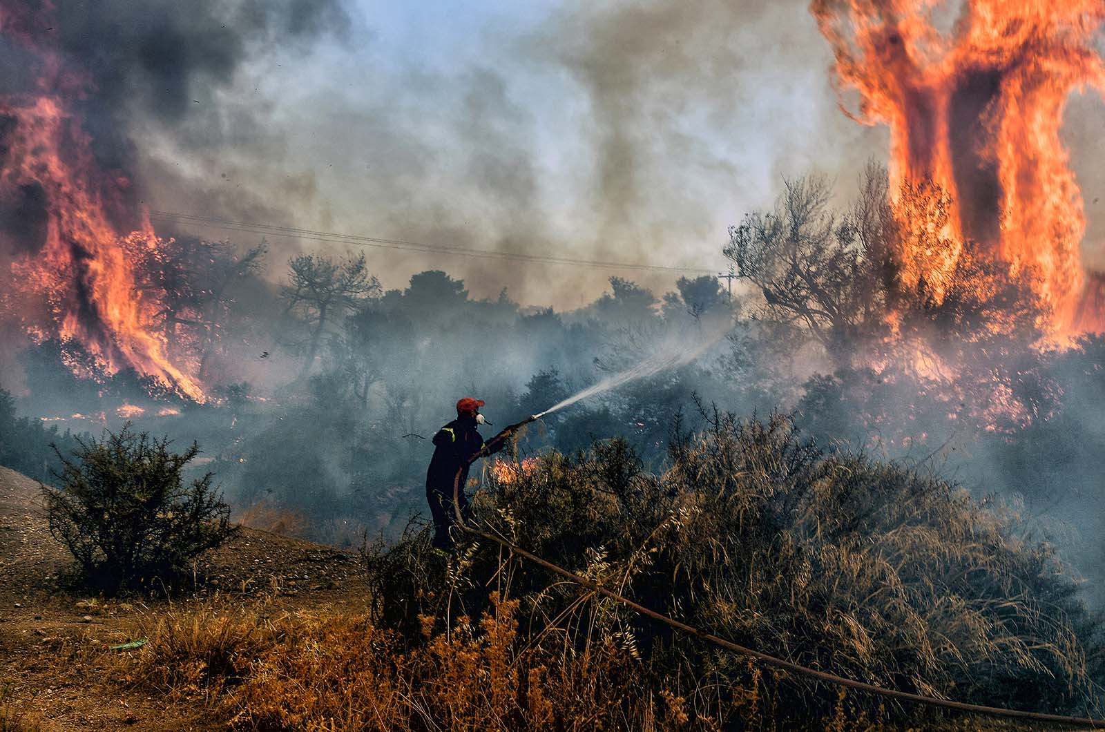 A fireman douses flames on a wildfire near Agioi Theodori, west of Athens, Greece - 18 July, 2023.