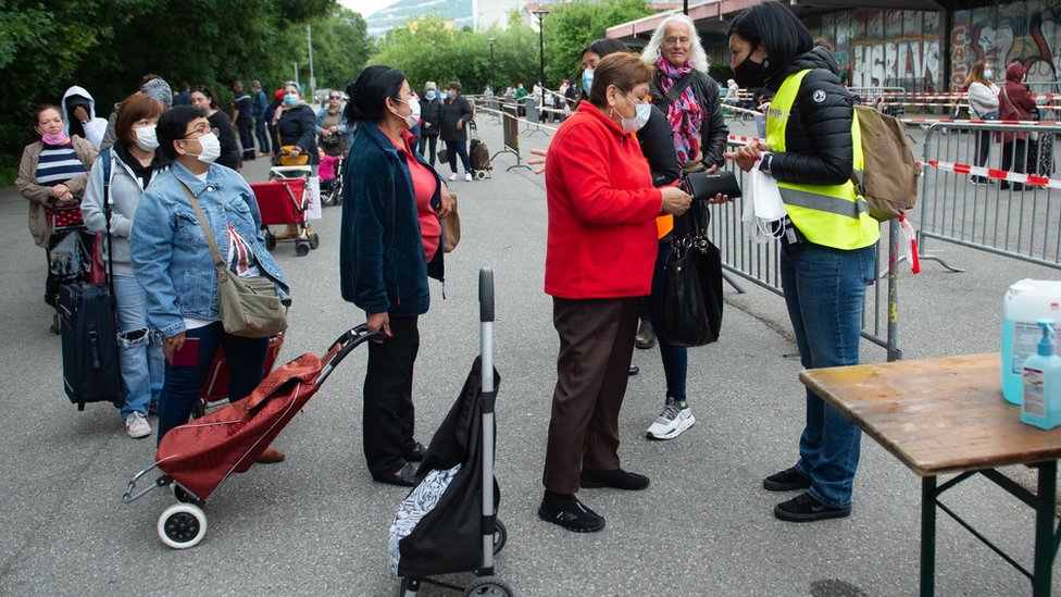 People wait in line to receive food parcels at a food bank in an ice rink during the coronavirus crisis on June 6, 2020 in Geneva