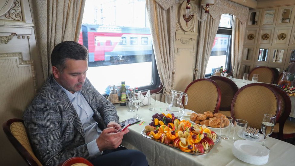 Un hombre revisa su teléfono celular frente a una mesa de uno de los restaurantes en el tren Zarengold. Un hombre revisa su teléfono celular frente a una mesa de uno de los restaurantes en el tren Zarengold.