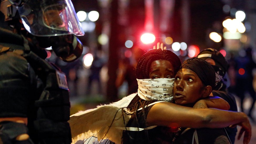 Две женщины обнялись, глядя на полицейского в Шарлотте, Северная Каролина, во время акции протеста 21 сентября