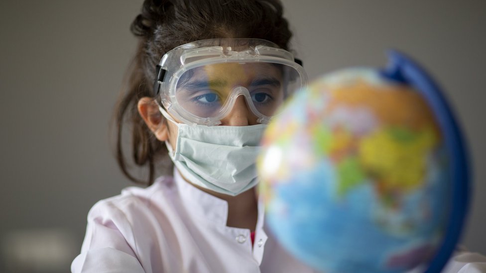 Menina usando máscara e óculos de proteção diante de globo terrestre