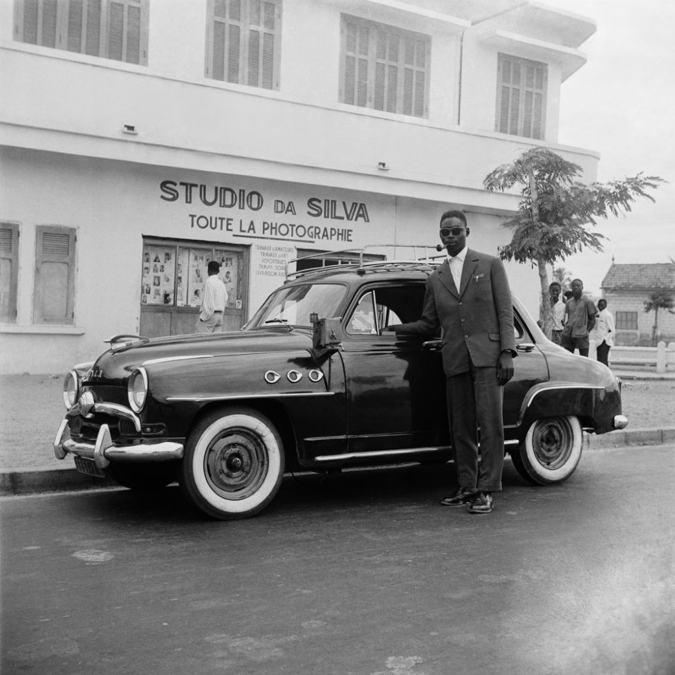A sharply dressed chauffeur poses with his vehicle outside Roger DaSilva's studio.