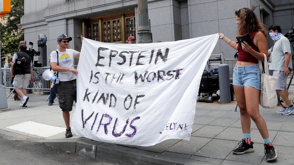 Un hombre y una mujer sujetan un cartel que dice: "Epstein es el peor tipo de virus".
