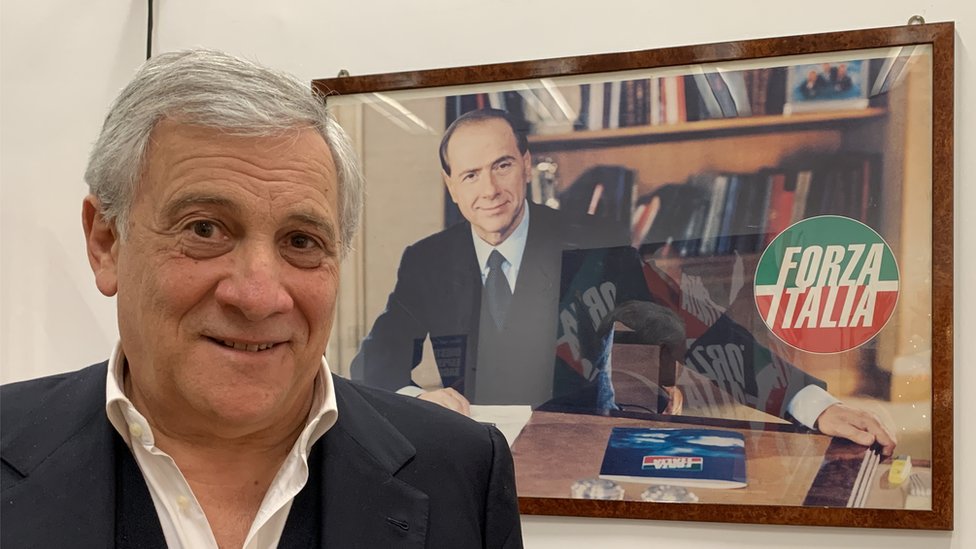 Antonio Tajani beneath a youthful picture of Silvio Berlusconi