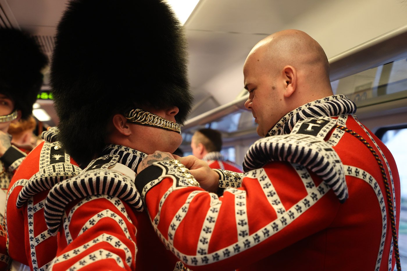A member of the Armed Forces has his uniform adjusted on a train into London
