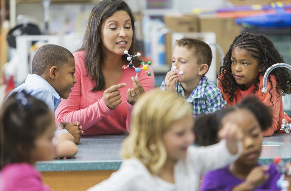Los maestros que mantienen relaciones más positivas con sus estudiantes, parecen influir en más altos niveles de trabajo en equipo. Una maestra con un grupo de alumnos.