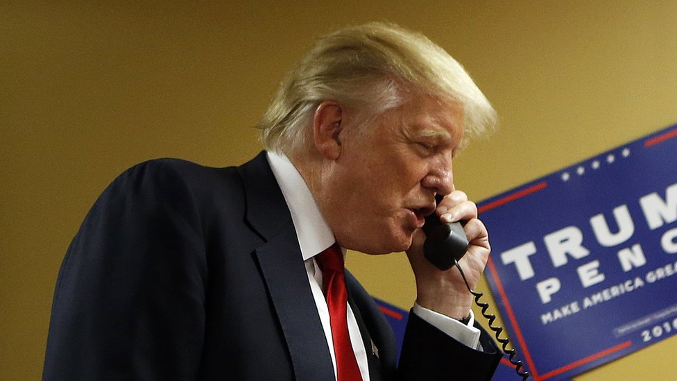 Кандидат в президенты от республиканцев Дональд Трамп разговаривает с абонентом на другом конце телефонной линии, пока волонтеры обслуживают телефонный банк перед митингом 12 сентября 2016 года.