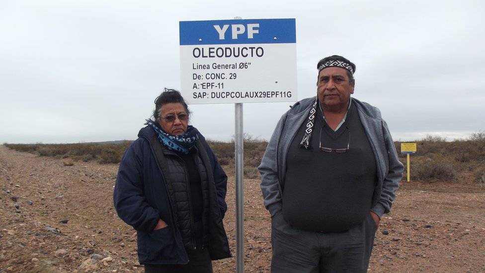 Джосифа и Альбино Кампо стоят перед вывеской нефтепровода YPF