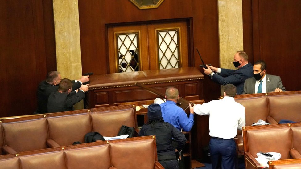 Law enforcement officers point their guns at a door that was vandalised in the House Chamber during a joint session of Congress in Washington DC, 6 January 2021