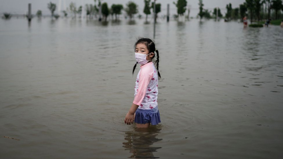 A little girl wearing a mask at a flooded street in China