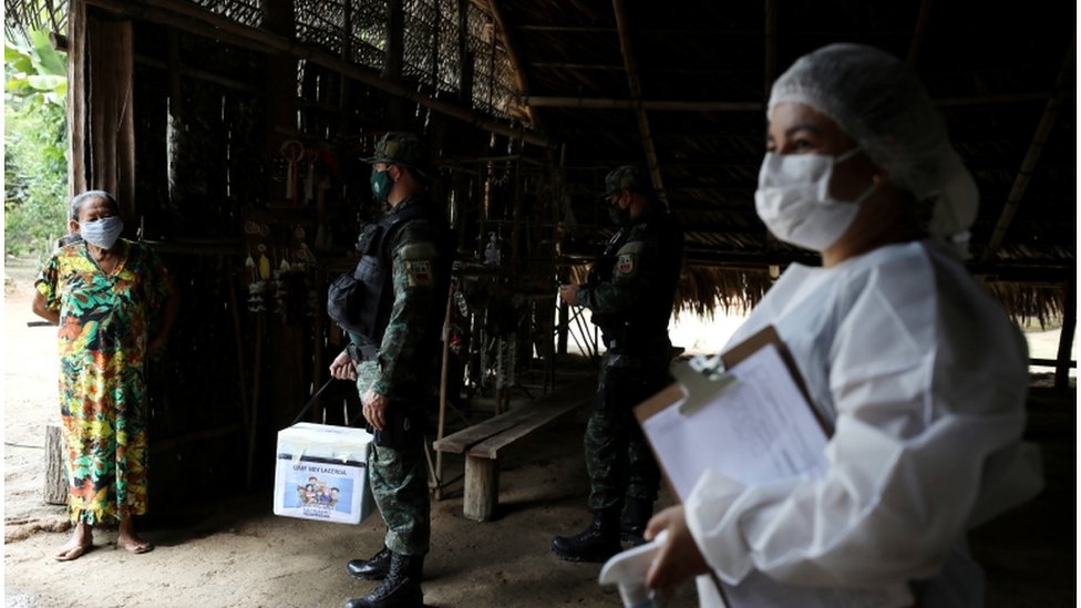 Uma trabalhadora de saúde municipal e um militar conversam com mulher indígena antes de ministrar uma vacina contra a covid nela no dia 9 de fevereiro de 2021, perto de Manaus